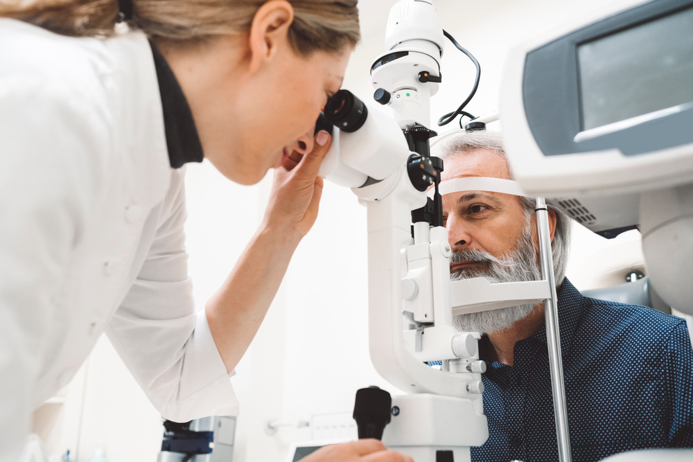 Ein Optiker führt eine Angiographie am Auge durch und untersucht die Augen eines älteren Mannes mit einer Spaltlampe in einer Klinik.