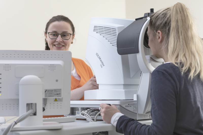 Eine Frau wird einer Augenuntersuchung unterzogen, während ein Team von Mitarbeitern des Gesundheitswesens Diagnosegeräte bedient und lächelt.
