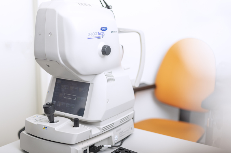 Nahaufnahme einer Augenuntersuchungsmaschine in einer Klinik, mit einem orangefarbenen Stuhl und einem Teamarbeitsplatz im Hintergrund.